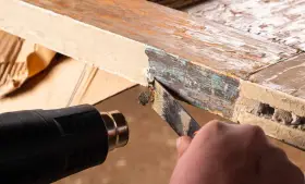 Se usa una pistola de calor para ablandar pintura vieja y descascarada de un marco de madera, facilitando su retirada con una espátula. La madera se hincha con el calor.