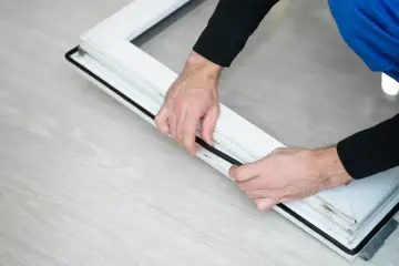Man installing a black rubber seal on a white window frame, demonstrating como poner burletes en ventanas correderas.