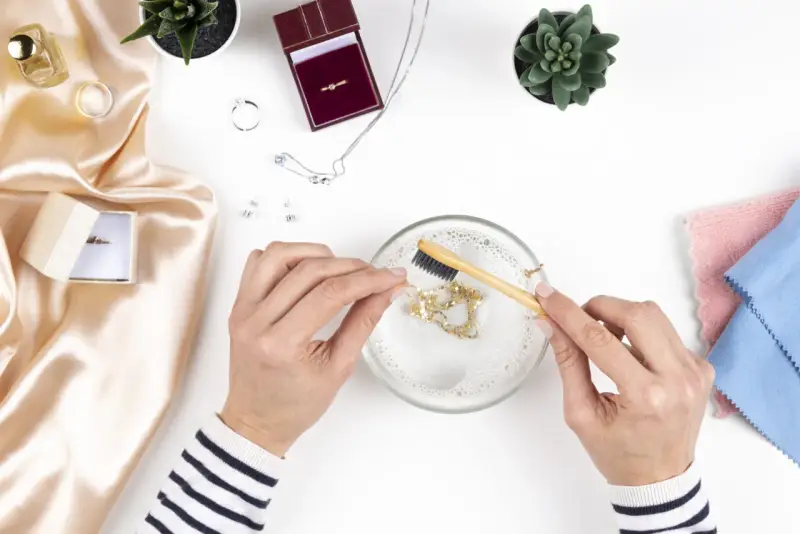 Manos limpian una cadena de oro con un cepillo en agua jabonosa. Aprende como limpiar el oro para que brille como nuevo.