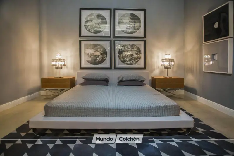 Cama moderna con cabecero tapizado, mesitas de noche de madera y lámparas de cristal. Cuadros decorativos en la pared y alfombra geométrica. Un espacio que invita a la armonía, ideal para aplicar principios de feng shui cama.