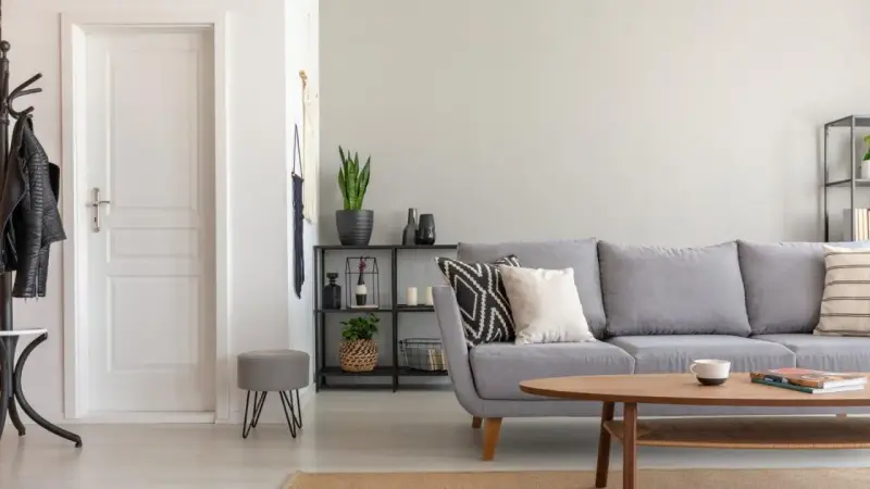 Un salón moderno con sofá gris, mesa de centro de madera y puerta blanca. El suelo claro ayuda a combinar suelo y puertas, creando un espacio luminoso.